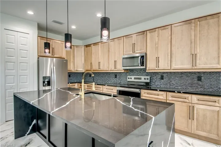 Kitchen with dark stone counters, stainless steel appliances, light tile flooring, backsplash, and hanging light fixtures
