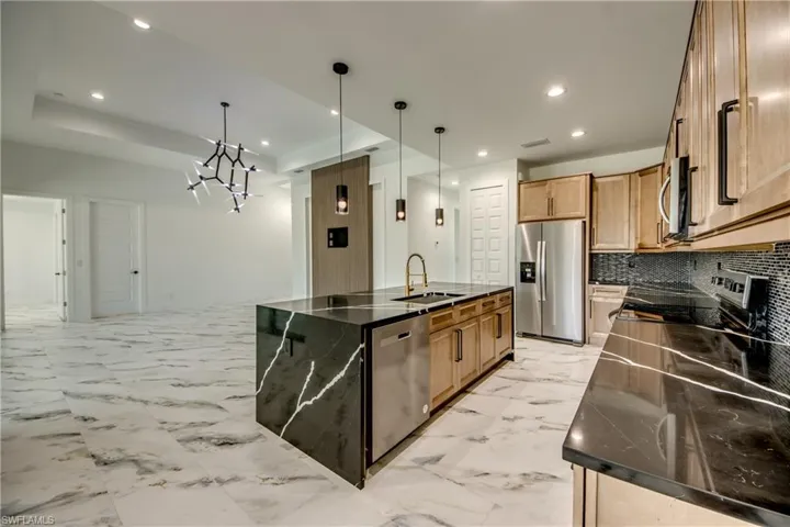 Kitchen featuring hanging light fixtures, appliances with stainless steel finishes, an island with sink, and light tile flooring