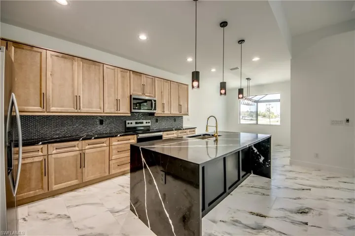 Kitchen featuring appliances with stainless steel finishes, tasteful backsplash, an island with sink, and light tile floors