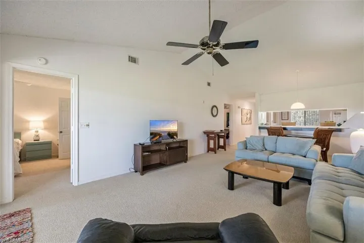 Living room with lofted ceiling, carpet flooring, a textured ceiling, and ceiling fan