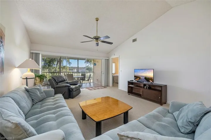 Carpeted living room with a textured ceiling, a ceiling fan, and high vaulted ceiling