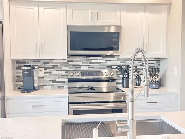 Kitchen with appliances with stainless steel finishes, decorative backsplash, white cabinets, and light stone counters