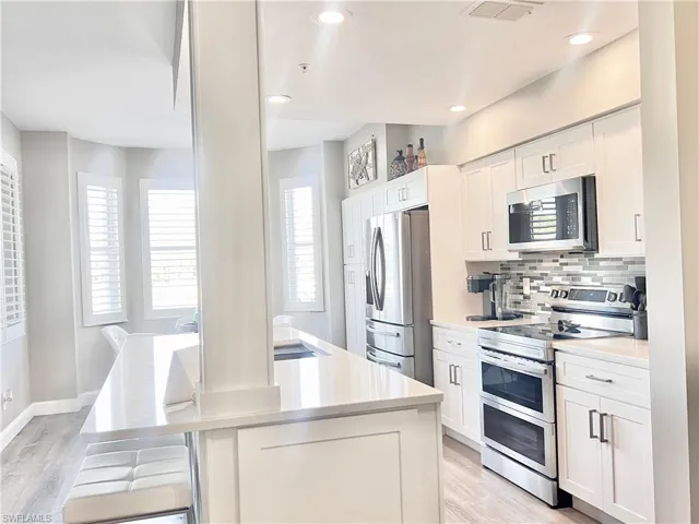 Kitchen featuring appliances with stainless steel finishes, white cabinetry, backsplash, light gray Deluxe Vinyl flooring, and recessed lighting