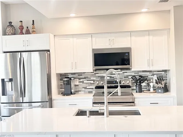 Kitchen featuring stainless steel appliances, white cabinetry, light stone counters, tasteful backsplash, and an island with sink