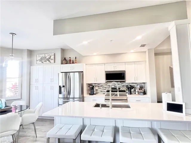 Kitchen with a breakfast bar area, white cabinetry, tasteful backsplash, stainless steel appliances, and decorative light fixtures