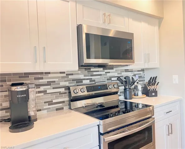 Kitchen with appliances with stainless steel finishes, white cabinetry, and decorative backsplash