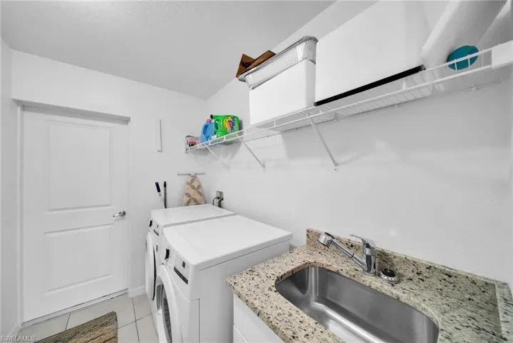Utility room featuring a stainless steel sink with a pull-down faucet, a light-colored granite-finish countertop, white wire shelving, and a paneled door