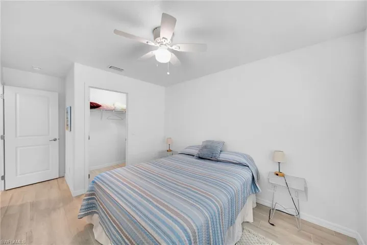 Bedroom featuring a ceiling fan with integrated lighting, wood-finish flooring, a white paneled door, and an open closet with wire shelving