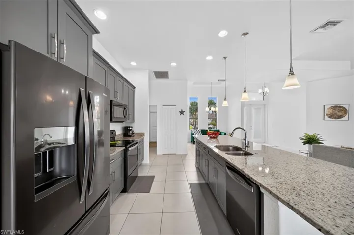 Open-concept kitchen featuring an extended island with a built-in sink, gray cabinetry, black stainless steel appliances, and recessed lighting