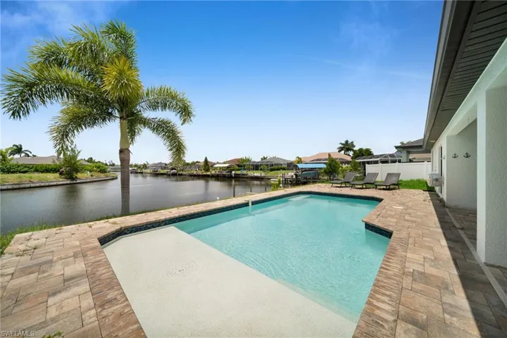 Waterfront pool area featuring a rectangular pool with sun shelf, paver surround, and mature palm tree