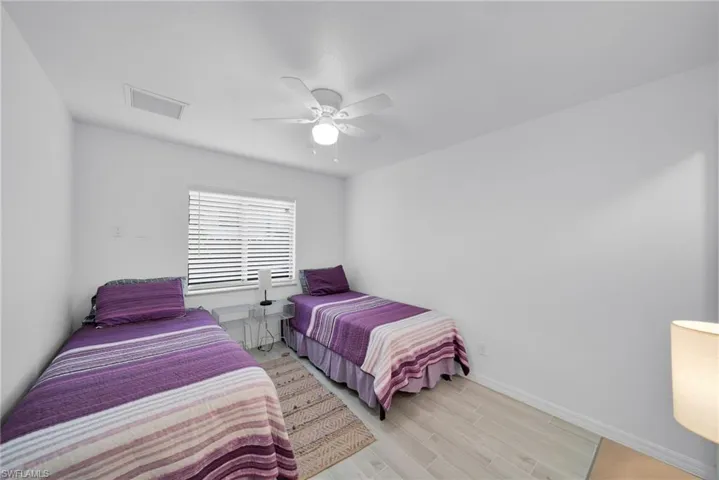 Bedroom featuring light-toned flooring, white walls, a window with horizontal blinds, and a ceiling fan with integrated lighting