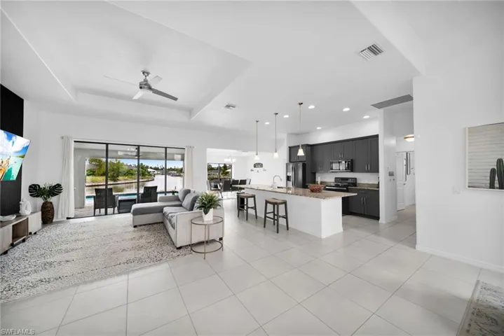 Open-concept living space featuring expansive glass sliding doors, tray ceilings with a ceiling fan, and large format tile flooring