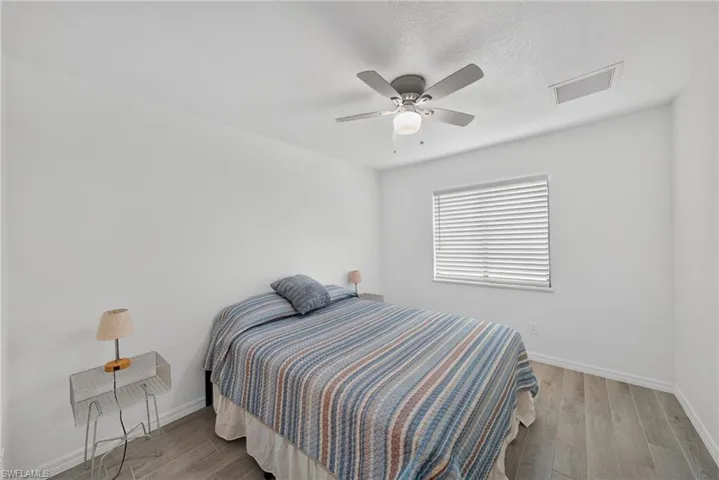 Bedroom featuring light-tone wood-finish flooring, a ceiling fan with integrated lighting, and a single window with horizontal blinds