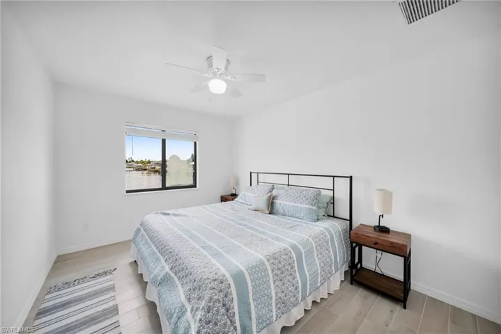Bedroom featuring a window with waterfront scenery, light-toned wood-finish flooring, a ceiling fan with integrated lighting, white walls, and white baseboards