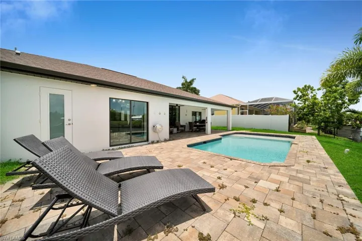 Outdoor living space featuring a rectangular swimming pool, paver patio, covered patio area, and expansive green lawn