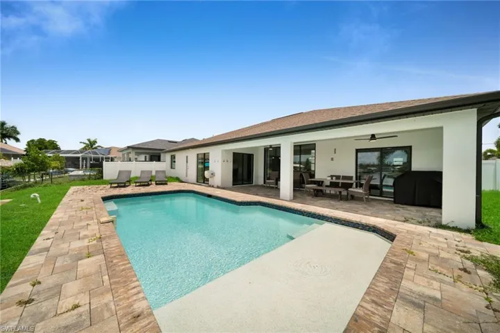Backyard featuring a rectangular swimming pool with an integrated sun shelf, surrounded by paver decking