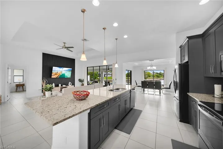 Open-concept kitchen featuring an island with light-toned countertop and pendant lighting, dark cabinetry, and white tile flooring