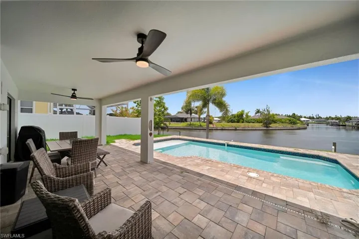 Covered lanai featuring paver flooring, two ceiling fans, an inground swimming pool, and waterfront access
