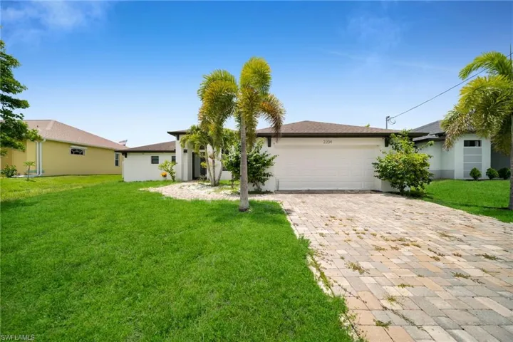 Contemporary stucco exterior with a two-car garage, paver driveway, and mature palm trees