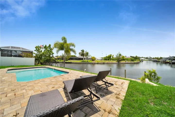 Waterfront backyard featuring a rectangular swimming pool, paver patio, lush green lawn, and mature palm trees