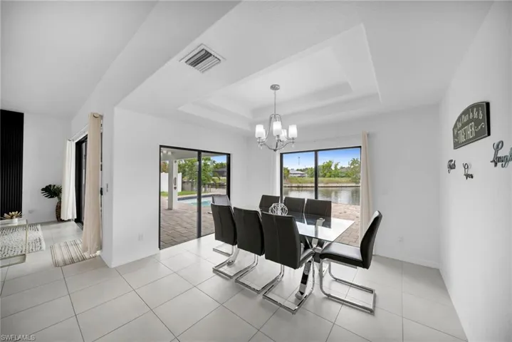 Dining area featuring a tray ceiling with a chandelier, tile flooring, and sliding glass doors opening to the exterior