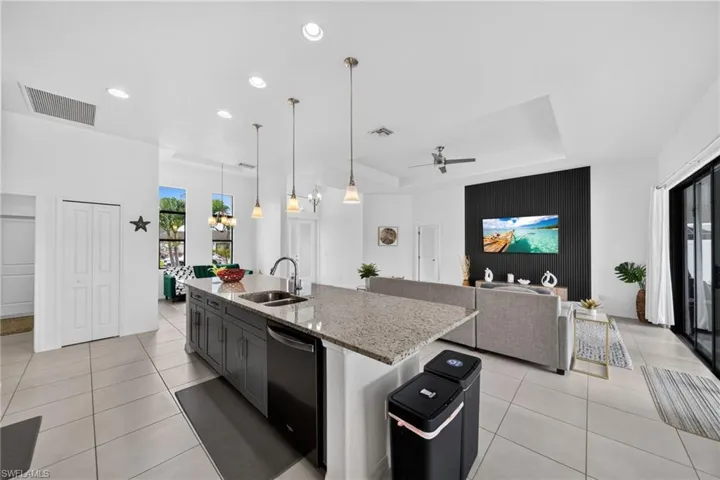 Open-concept kitchen featuring an island with a stainless steel sink and integrated dishwasher, pendant lighting, and light-toned tile flooring