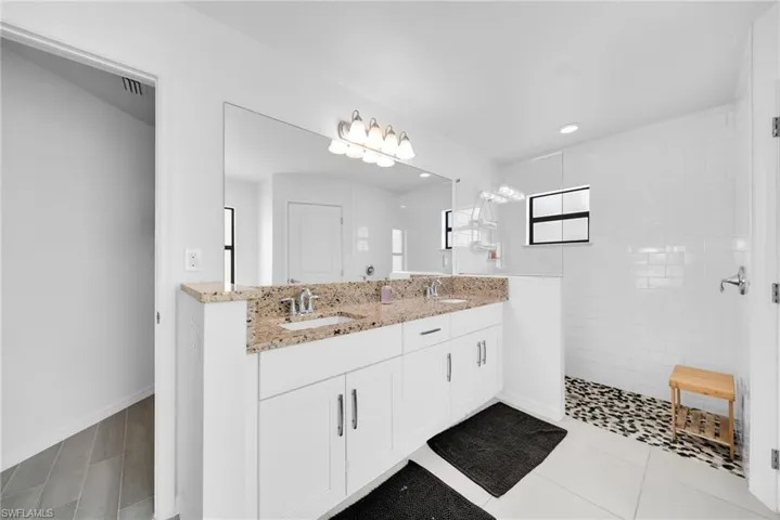 Double vanity with light granite countertops, polished chrome fixtures, and white cabinetry