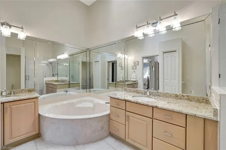 Primary bathroom featuring two vanities, a garden tub, light tile patterned flooring, a newly renovated stall shower, granite countertops and a high ceiling.