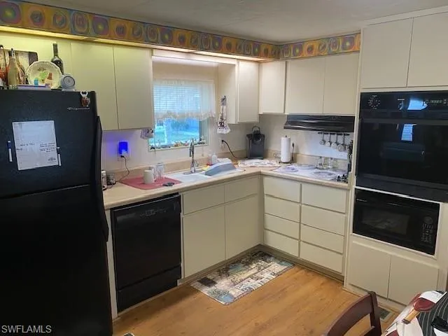 Kitchen featuring black appliances, light countertops, light wood-style floors, and white cabinetry