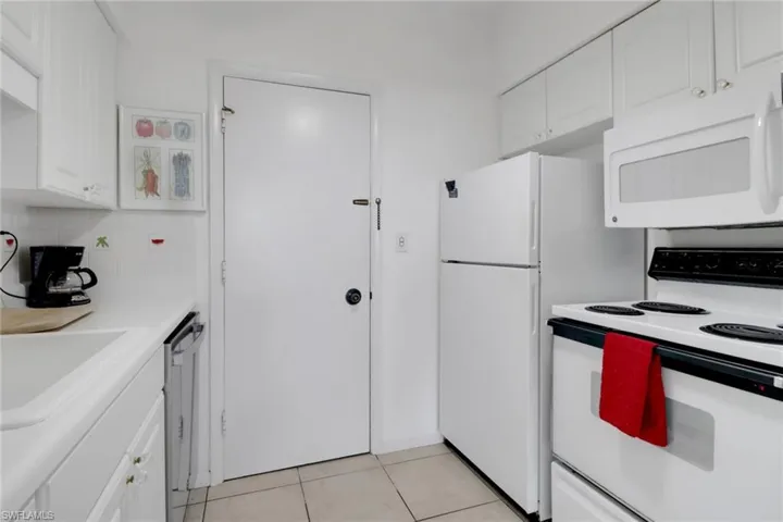 Kitchen featuring white appliances, light countertops, white cabinets, light tile patterned floors, and a sink