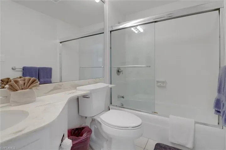 Bathroom with tile patterned flooring, vanity, combined bath / shower with glass door, and toilet