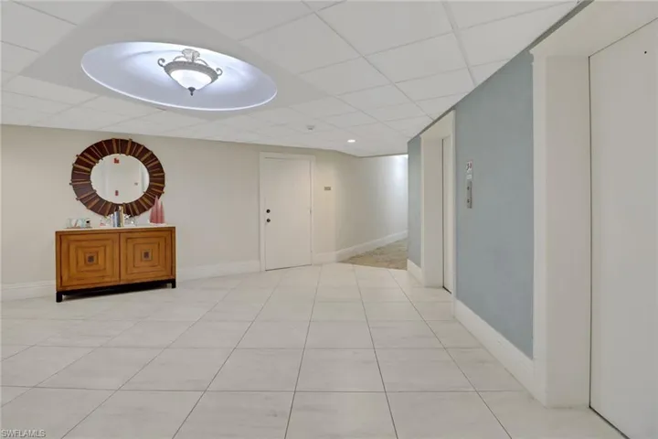 Hall with light tile patterned floors, a paneled ceiling, and baseboards
