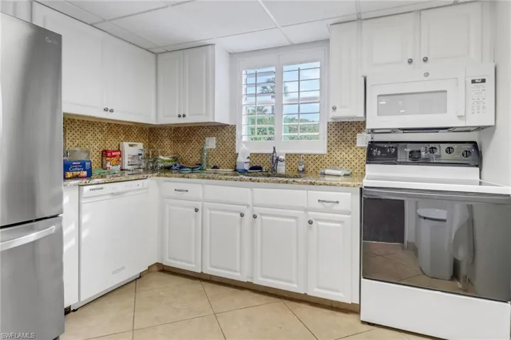 Kitchen with white appliances, white cabinets, decorative backsplash, and a drop ceiling
