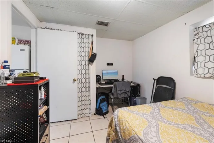Bedroom featuring an office area, a paneled ceiling, light tile patterned floors, and freestanding refrigerator