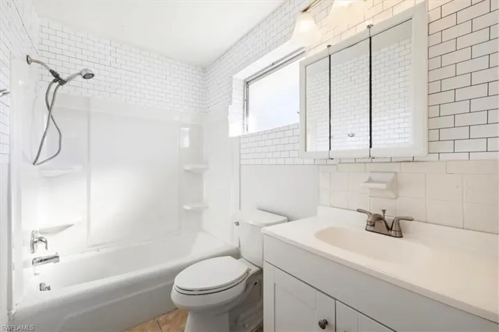 Full bathroom featuring shower / bathtub combination, tile walls, vanity, tasteful backsplash, and light tile patterned floors