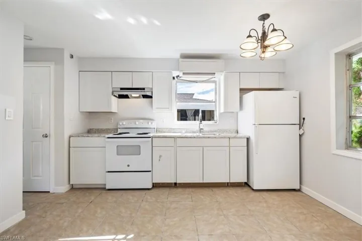 Kitchen with white appliances, white cabinetry, under cabinet range hood, decorative light fixtures, and light tile patterned floors