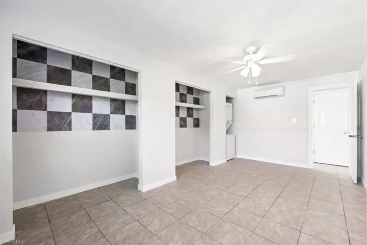 Unfurnished room with estacked washer and dryer, a wall mounted air conditioner, light tile patterned floors, and a ceiling fan
