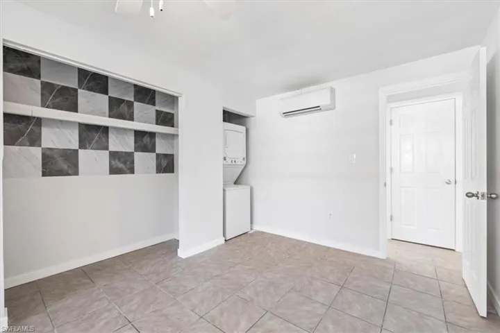 Unfurnished room featuring stacked washer and clothes dryer, a wall mounted AC, light tile patterned floors, and a ceiling fan