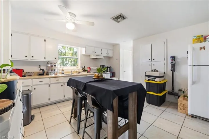 Kitchen with light tile patterned floors, freestanding refrigerator, white cabinetry, and light countertops