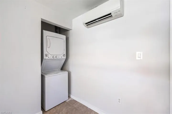 Laundry room featuring a wall mounted AC, light tile patterned floors, and stacked washer / drying machine