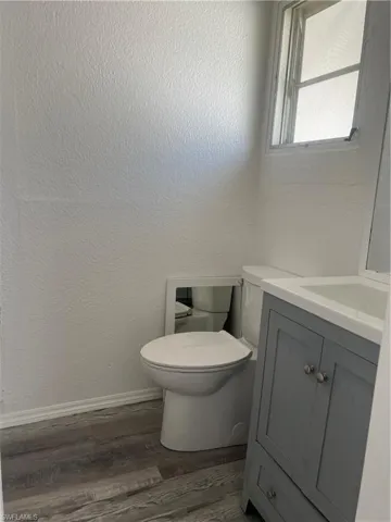 Half bathroom featuring baseboards, wood finished floors, vanity, and toilet