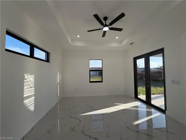Spare room with light marble finish flooring, plenty of natural light, ceiling fan, recessed lighting, and a tray ceiling