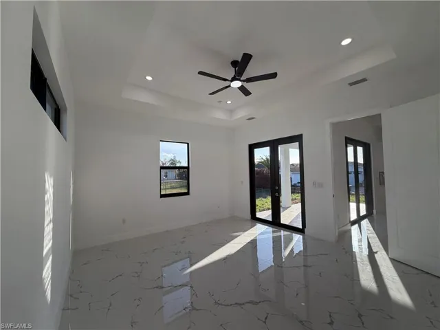 Empty room featuring french doors, recessed lighting, a ceiling fan, light marble finish floors, and a raised ceiling