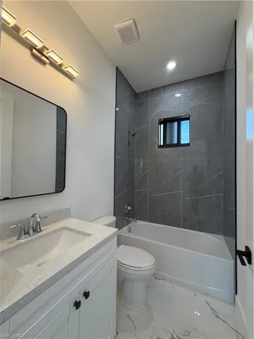 Full bathroom featuring vanity, shower / bath combination, light marble finish floors, and recessed lighting