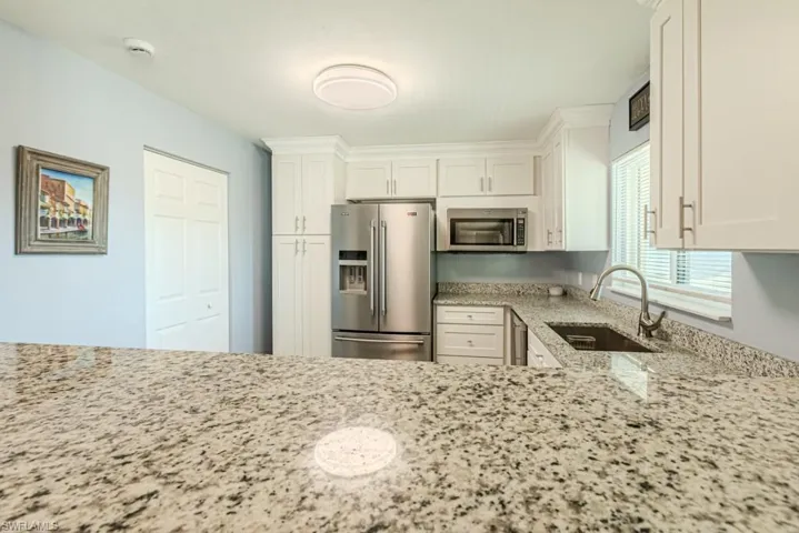 Kitchen with light stone countertops, sink, white cabinets, and stainless steel appliances