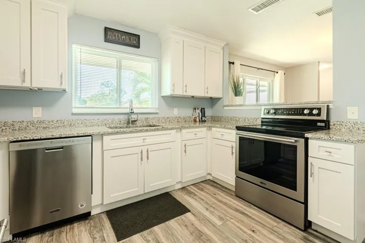 Kitchen with appliances with stainless steel finishes, white cabinetry, a healthy amount of sunlight, and light hardwood / wood-style floors
