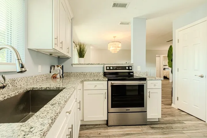 Kitchen with sink, white cabinets, stainless steel range with electric cooktop, and light hardwood / wood-style floors