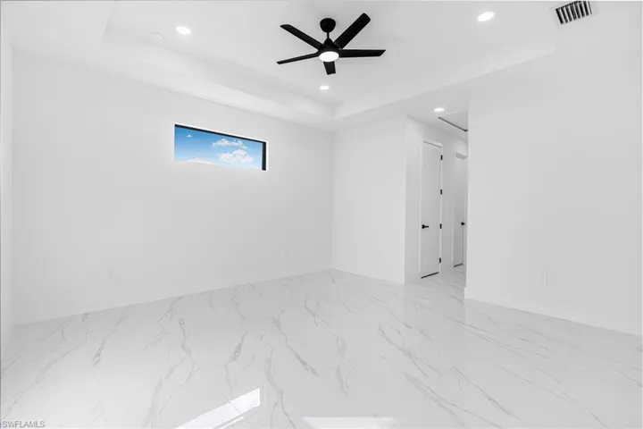 Empty room with a raised ceiling, ceiling fan, recessed lighting, and light marble finish floors