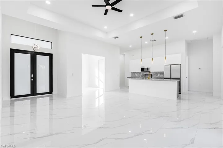 Unfurnished living room with ceiling fan, a high tray ceiling, light marble finish flooring, recessed lighting, and french doors