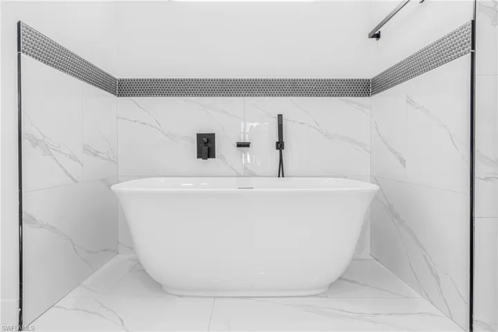 Bathroom featuring light marble finish floors and a freestanding tub